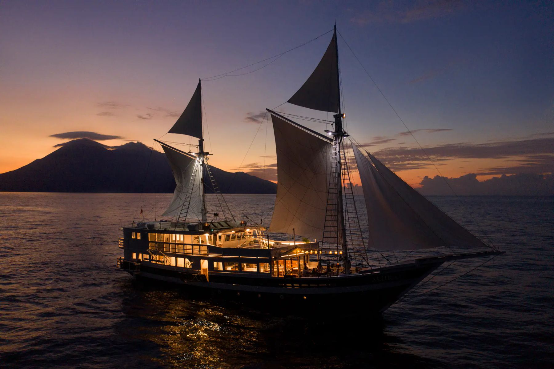 Phinisi lit up at dusk under full sail, Indonesia